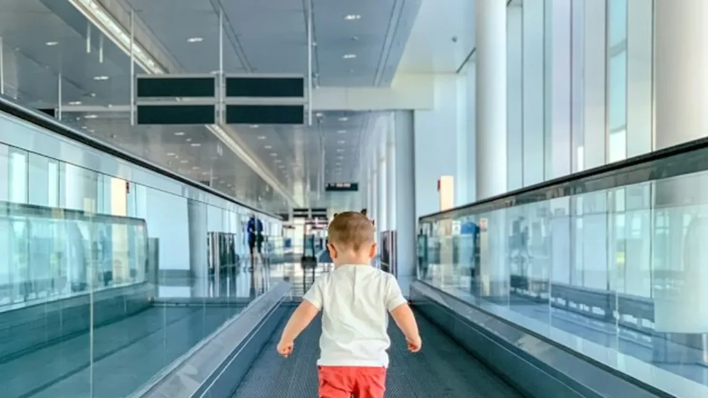 A toddler walking ahead on an airport moving walkway, seen from behind