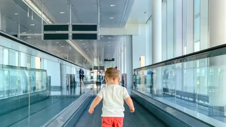 A toddler walking ahead on an airport moving walkway, seen from behind